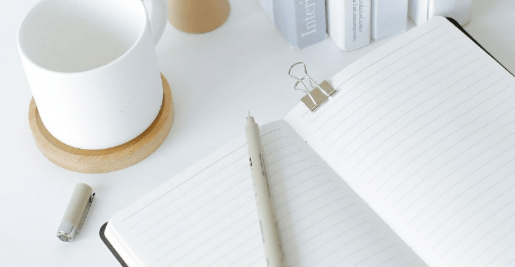 An open note book, pen and white coffee cup.